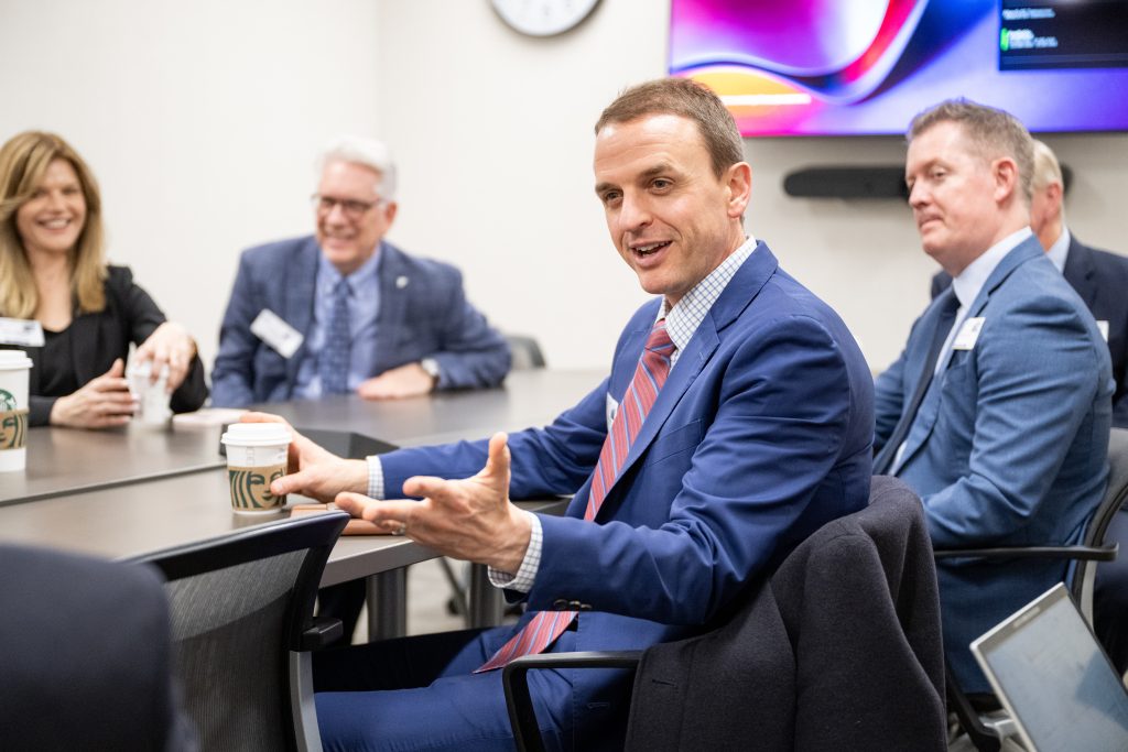 A conference room with people in business attire seated at a table and speaking with one another
